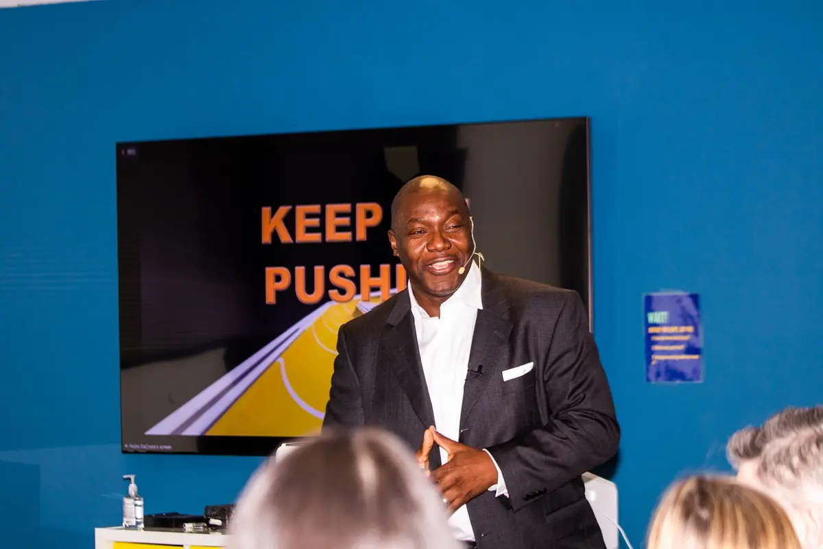 Sales kickoff keynote speaker Devon Harris on stage in front of a Keep On Pushing slide at a company kickoff week