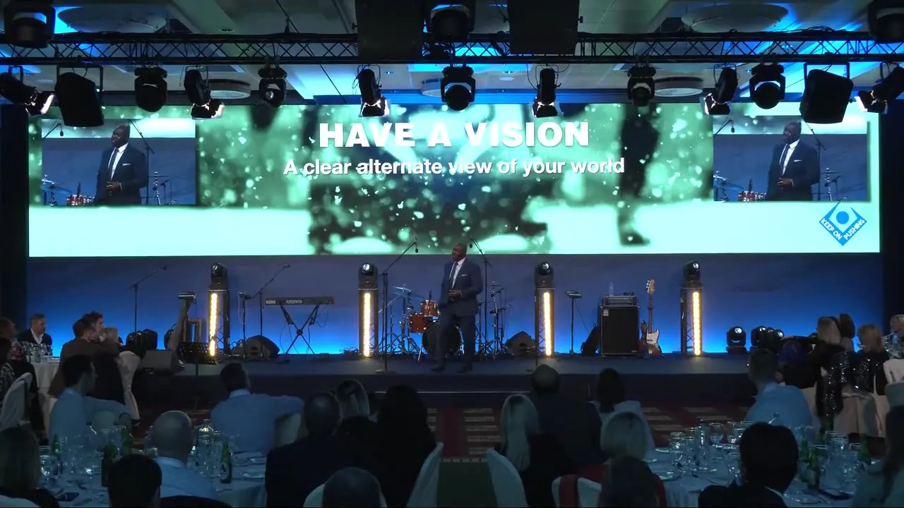 Devon Harris on stage at a leadership meeting in front of a Have a Vision slide