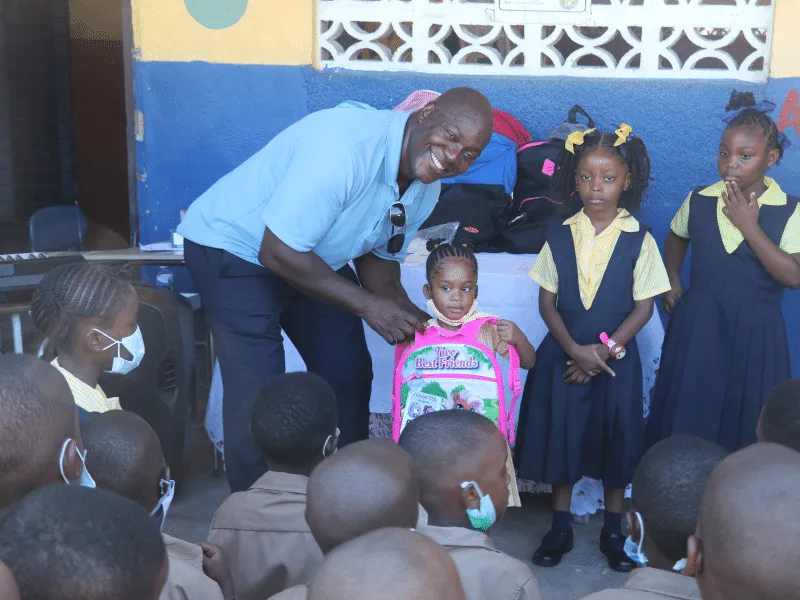 Devon Harris handing a new book bag to a student in Kingston